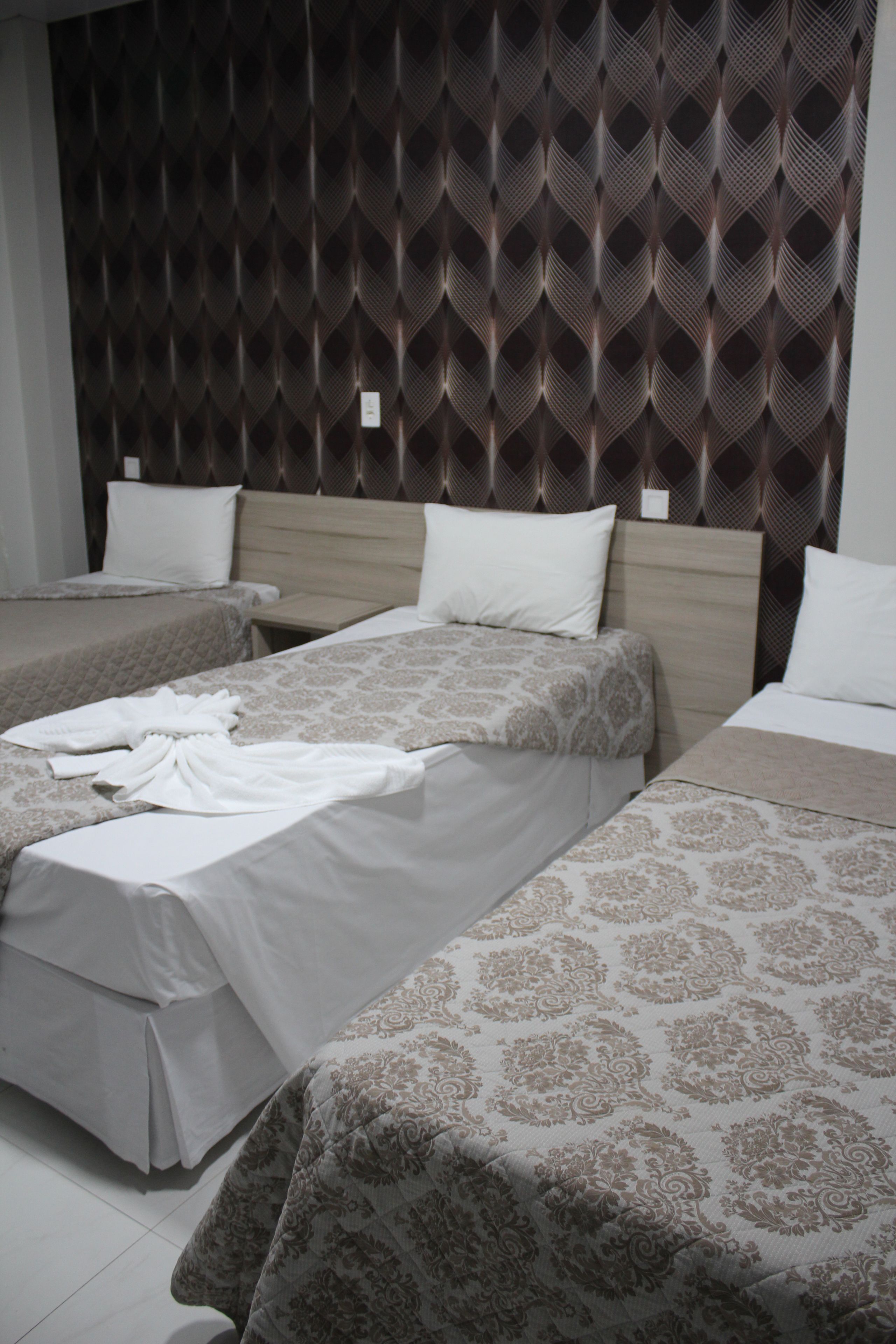 A hotel room with three beds, each with a different patterned bedspread.