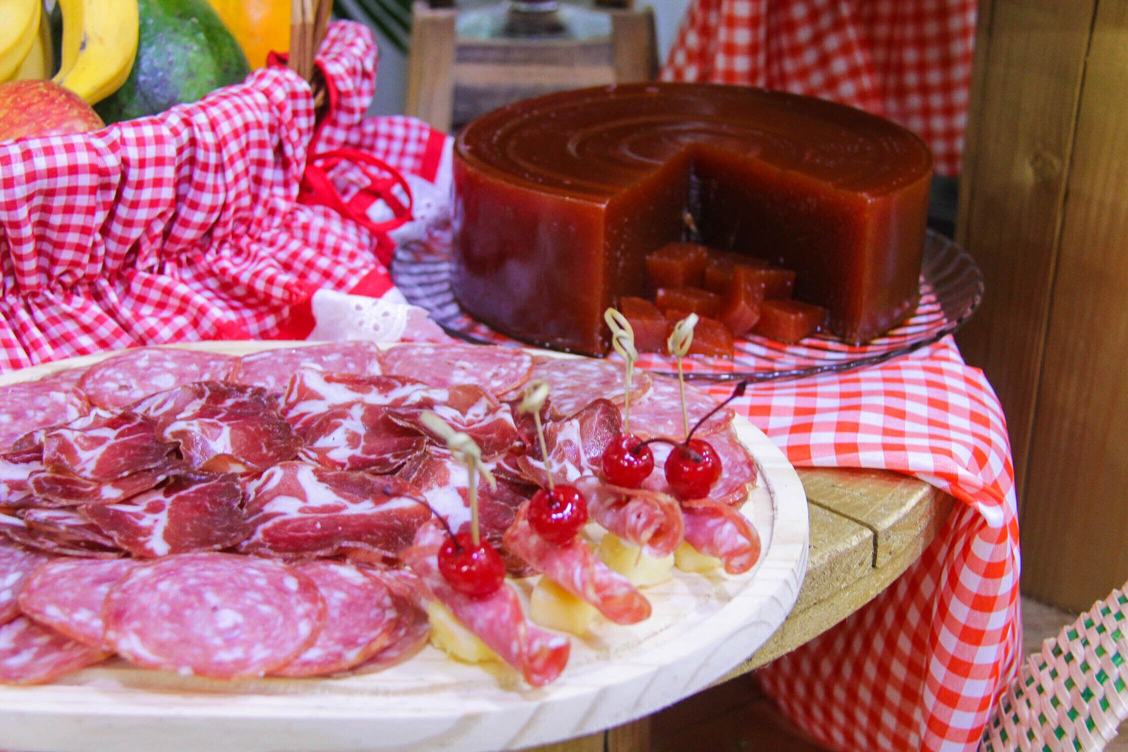 A charcuterie board with various meats, cheeses, and fruits on a checkered tablecloth.