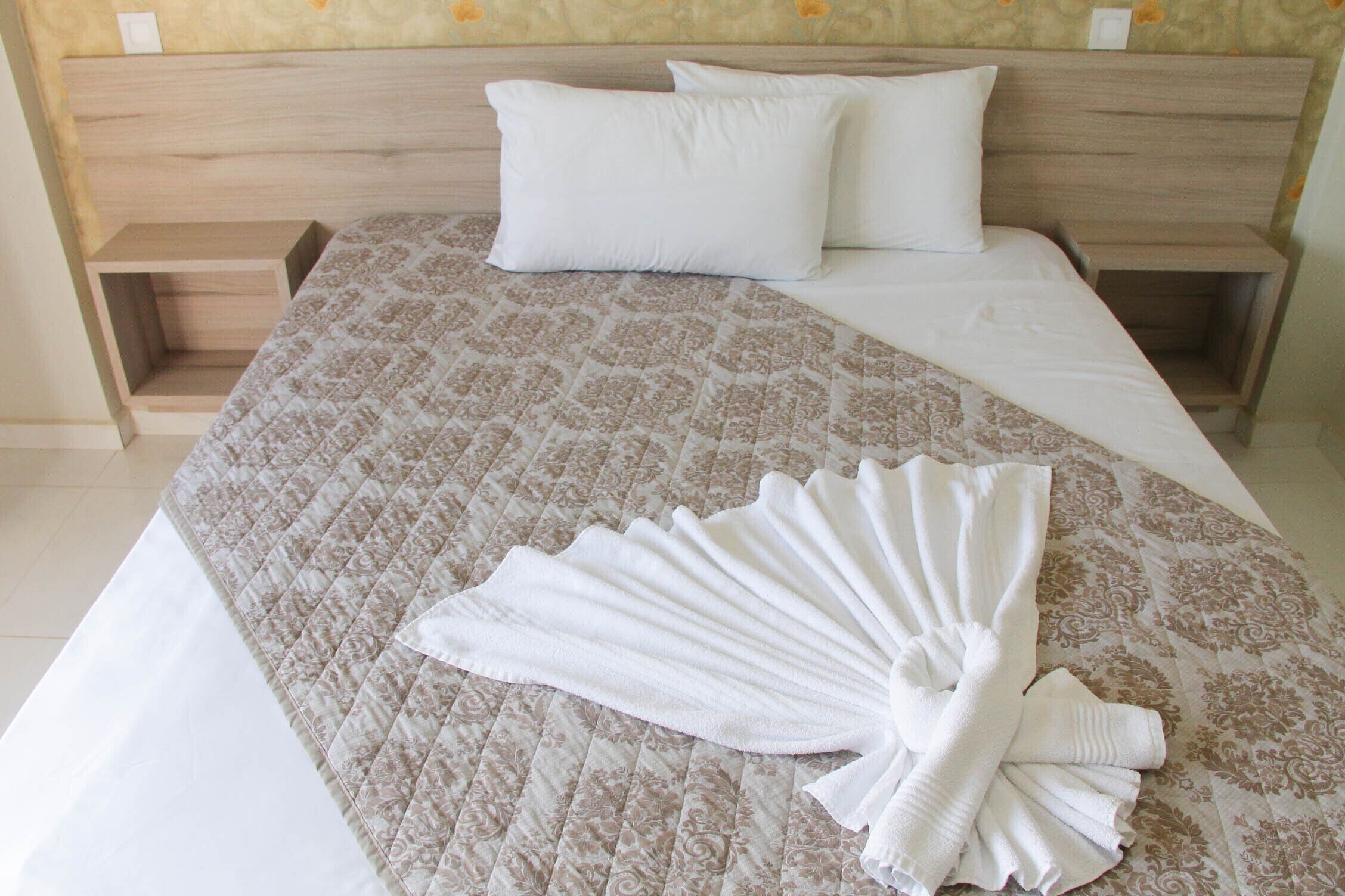 Una cama bien hecha con una colcha estampada, dos almohadas y una toalla doblada sobre la cama.