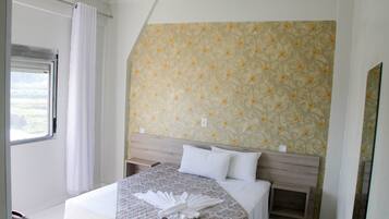 A hotel room with a bed, a headboard, a window with curtains, and a wall with a floral pattern.