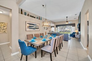 Uma sala de jantar espaçosa com mesa de madeira posta para seis pessoas, rodeada por cadeiras estofadas em azul.