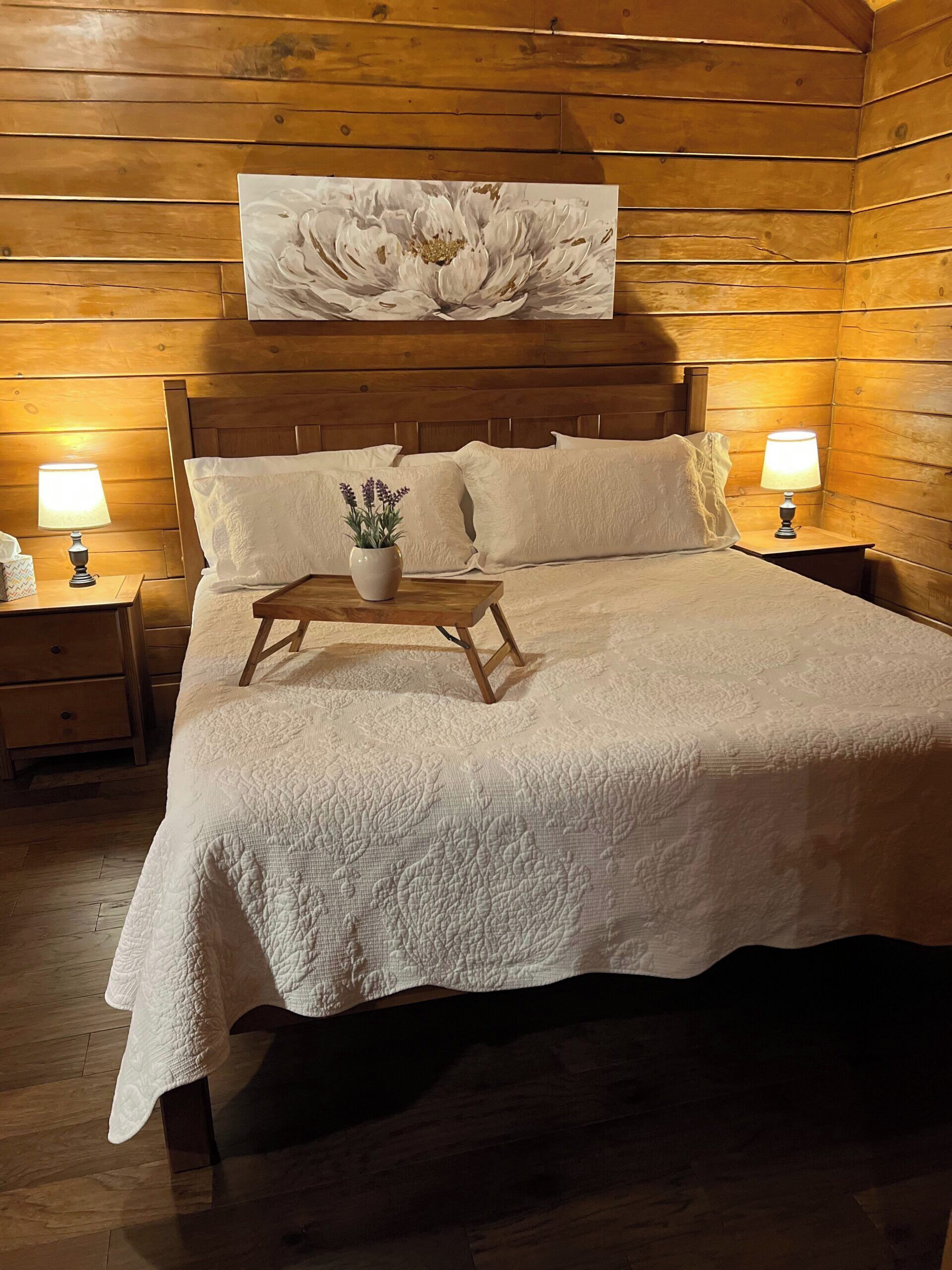 Quarto com painéis de madeira, uma cama grande, duas mesas de cabeceira com abajures e uma obra de arte pendurada na parede.