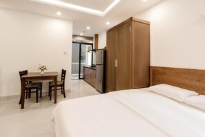 Habitació d'hotel amb un llit, un armari de fusta, una taula de dinar amb cadires i un frigorífic.