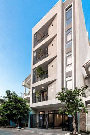 Un edifici de diverses plantes amb balcons, una entrada tancada per reixa i un cel clar.