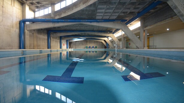 An indoor swimming pool with clear lanes, a tiled floor, and a high ceiling with visible structural beams. - Parque Botanico Holiday Rentals (Estepona)