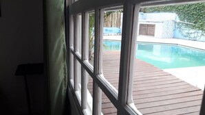 Vista desde el interior de una habitación hacia una terraza de madera con piscina.