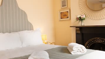 A neatly made bed with pillows and a folded towel, a bedside lamp, a framed picture, and a mirror on the wall.