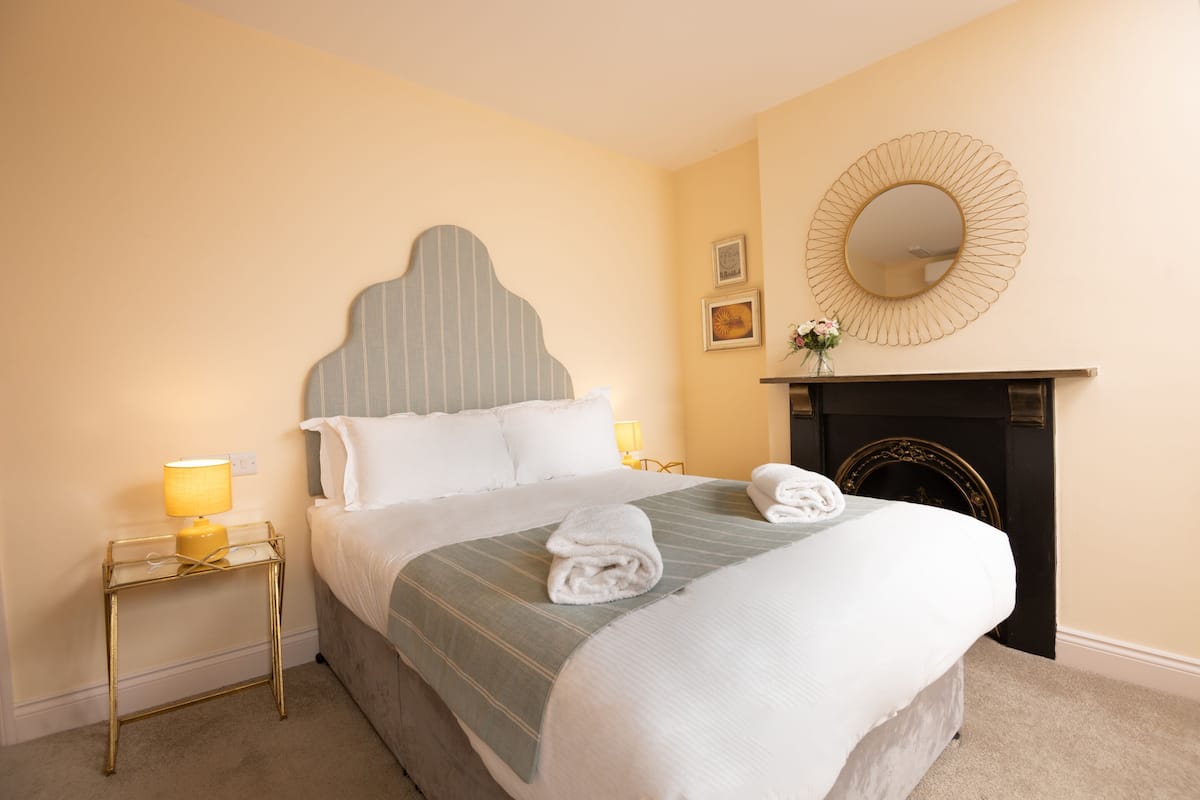 A neatly made bed with a striped bedspread, a bedside lamp, and a mirror on the wall.