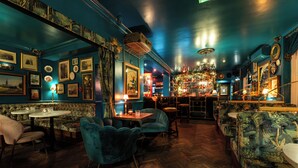 Un bar au sol en bois et aux murs bleus, avec des tabourets, des tables et des tableaux encadrés.