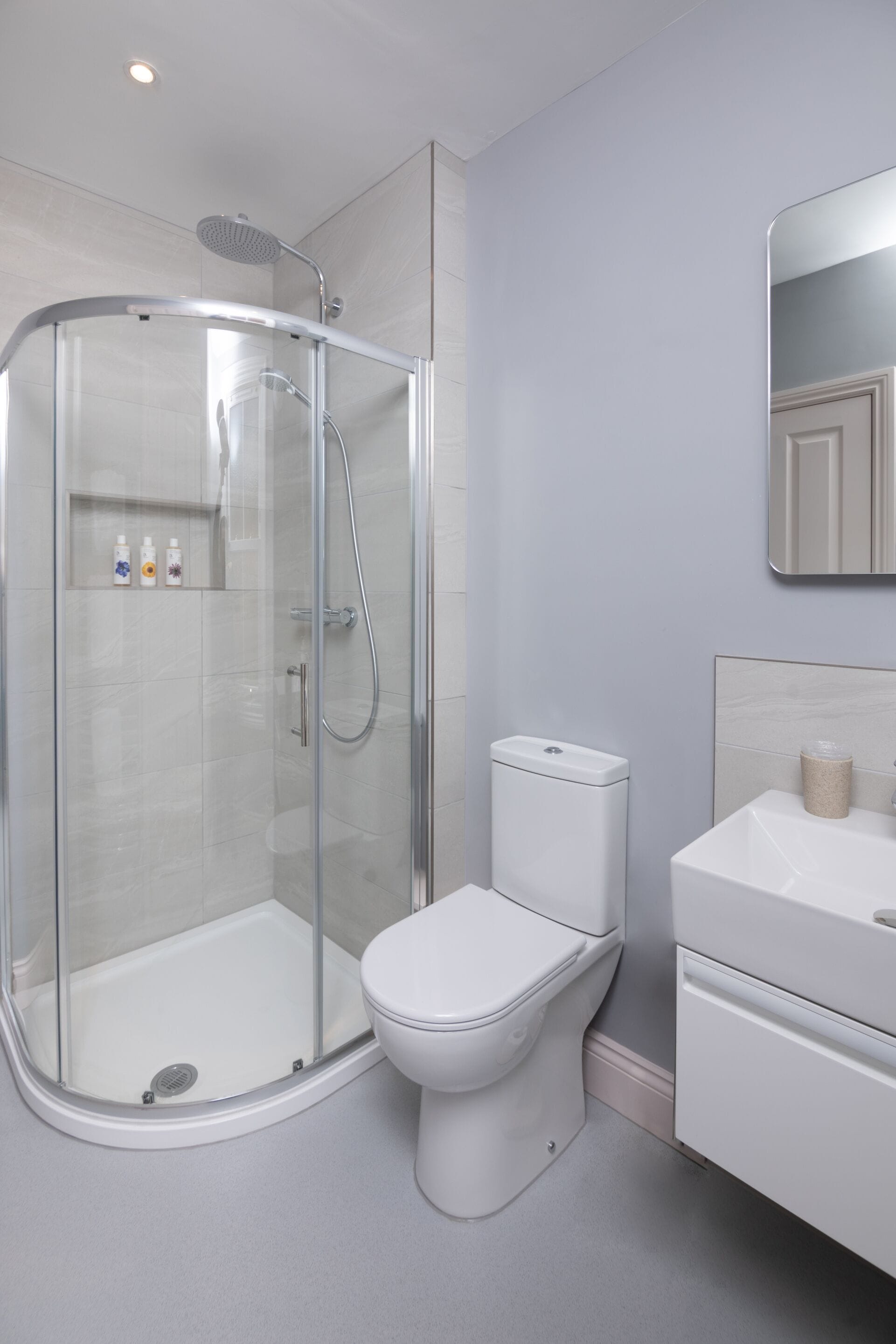 A modern bathroom with a glass-enclosed shower, a white toilet, and a vanity with a mirror.
