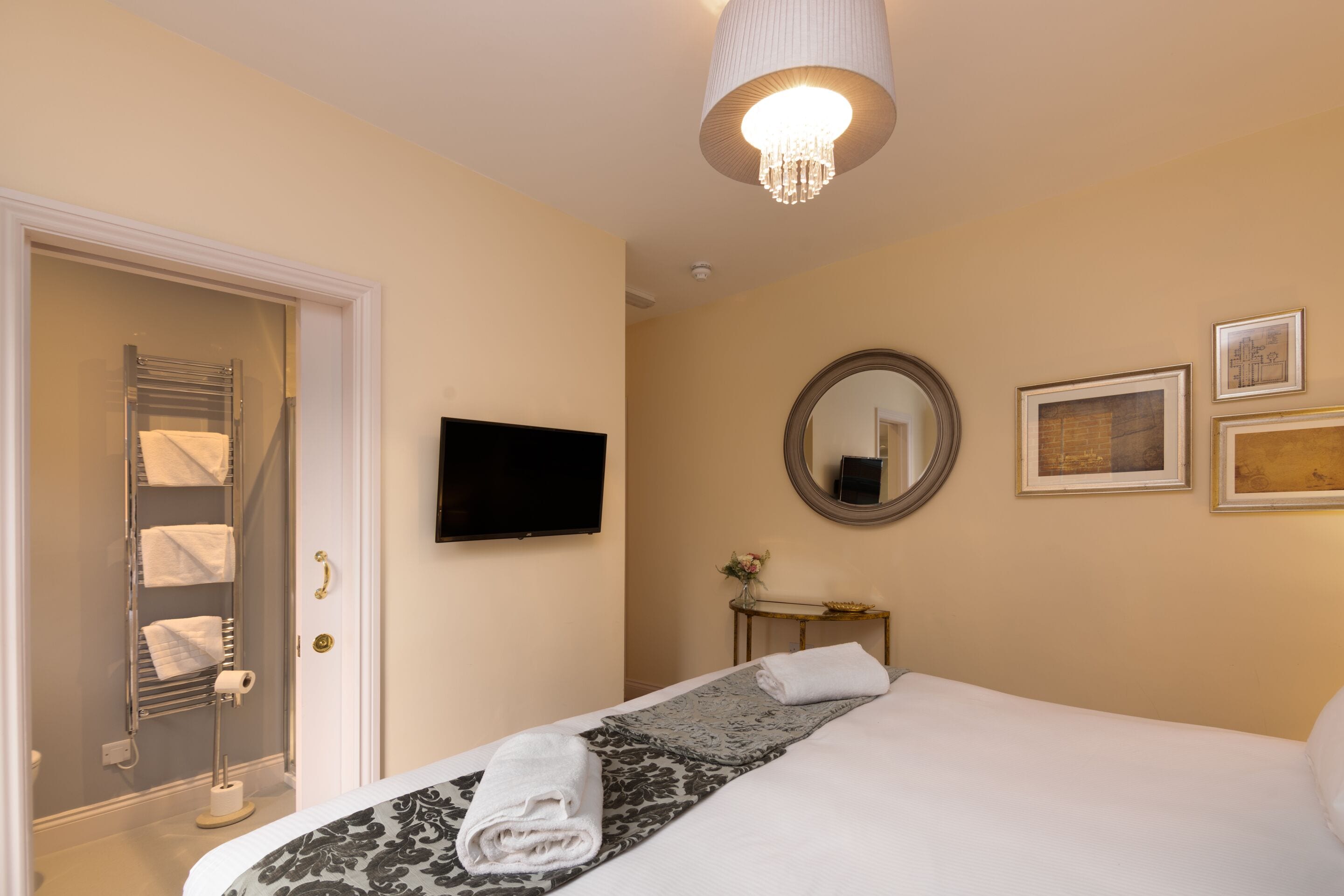 A hotel room with a bed, a television, a mirror, and framed artwork on the wall.