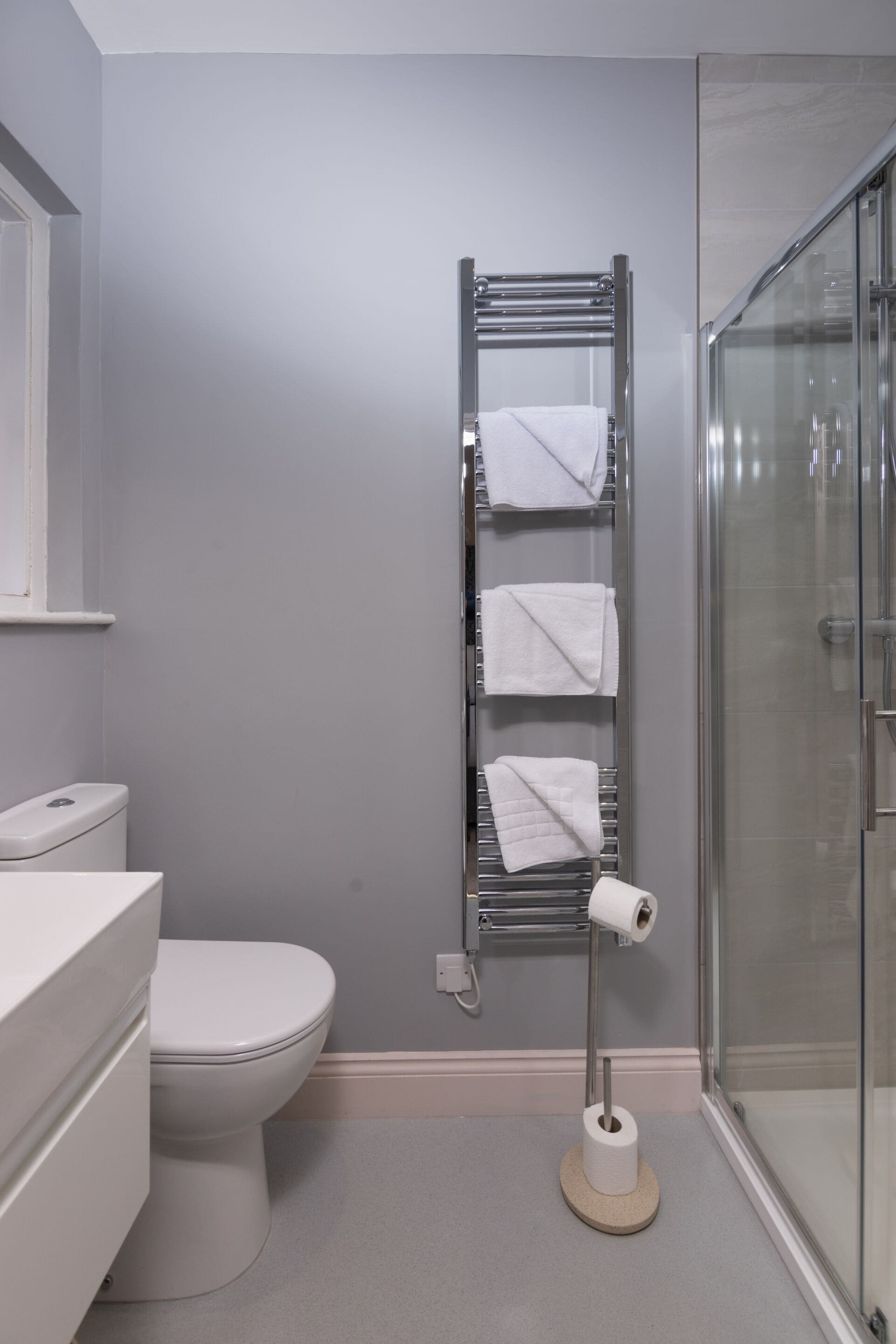 A bathroom with a toilet, a towel rack with towels, and a glass shower enclosure.