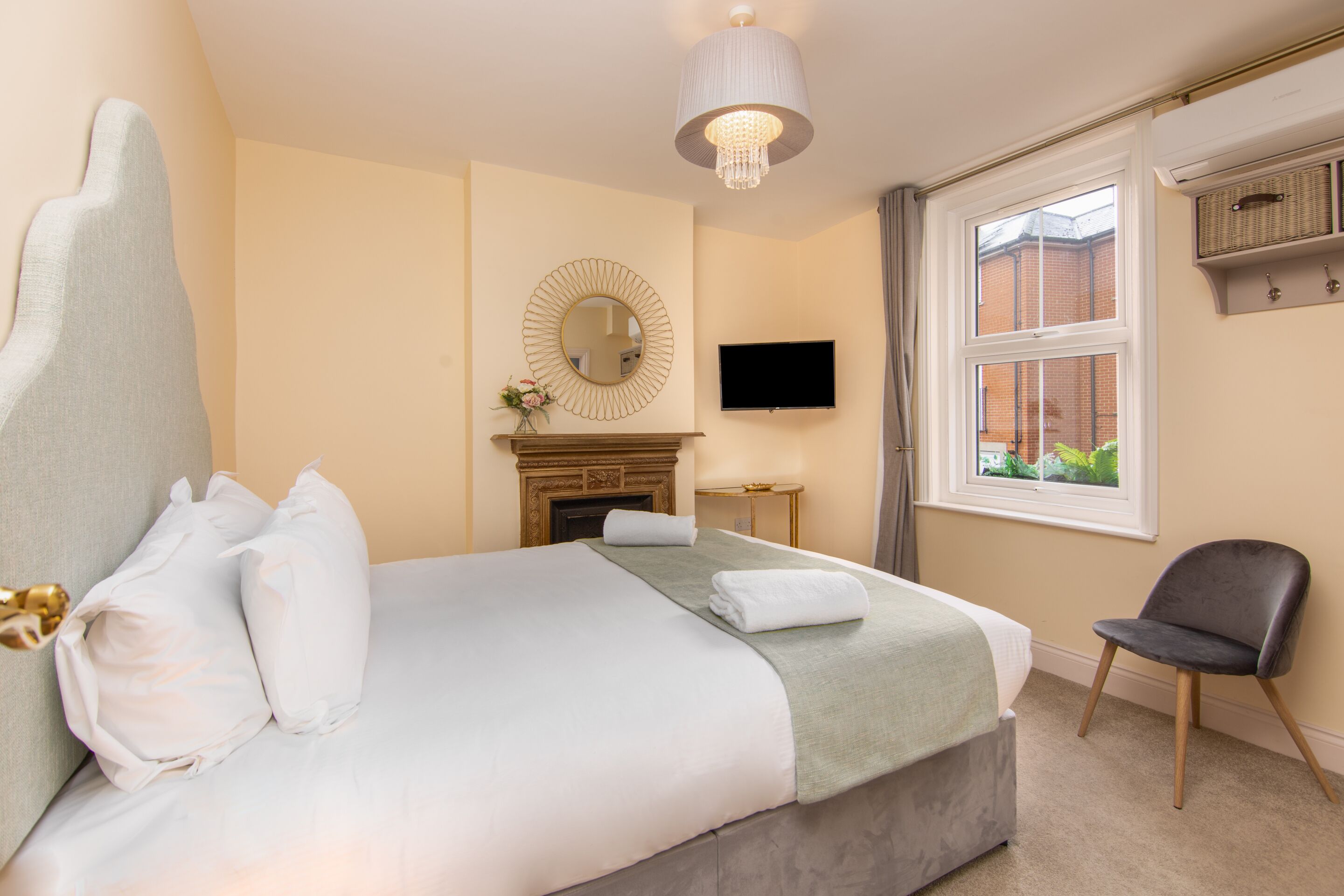 A hotel room with a bed, a television, a fireplace, a window, and a chair.