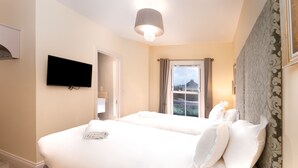Une chambre d’hôtel avec deux lits, un téléviseur à écran plat, un luminaire au plafond et une fenêtre avec des rideaux.