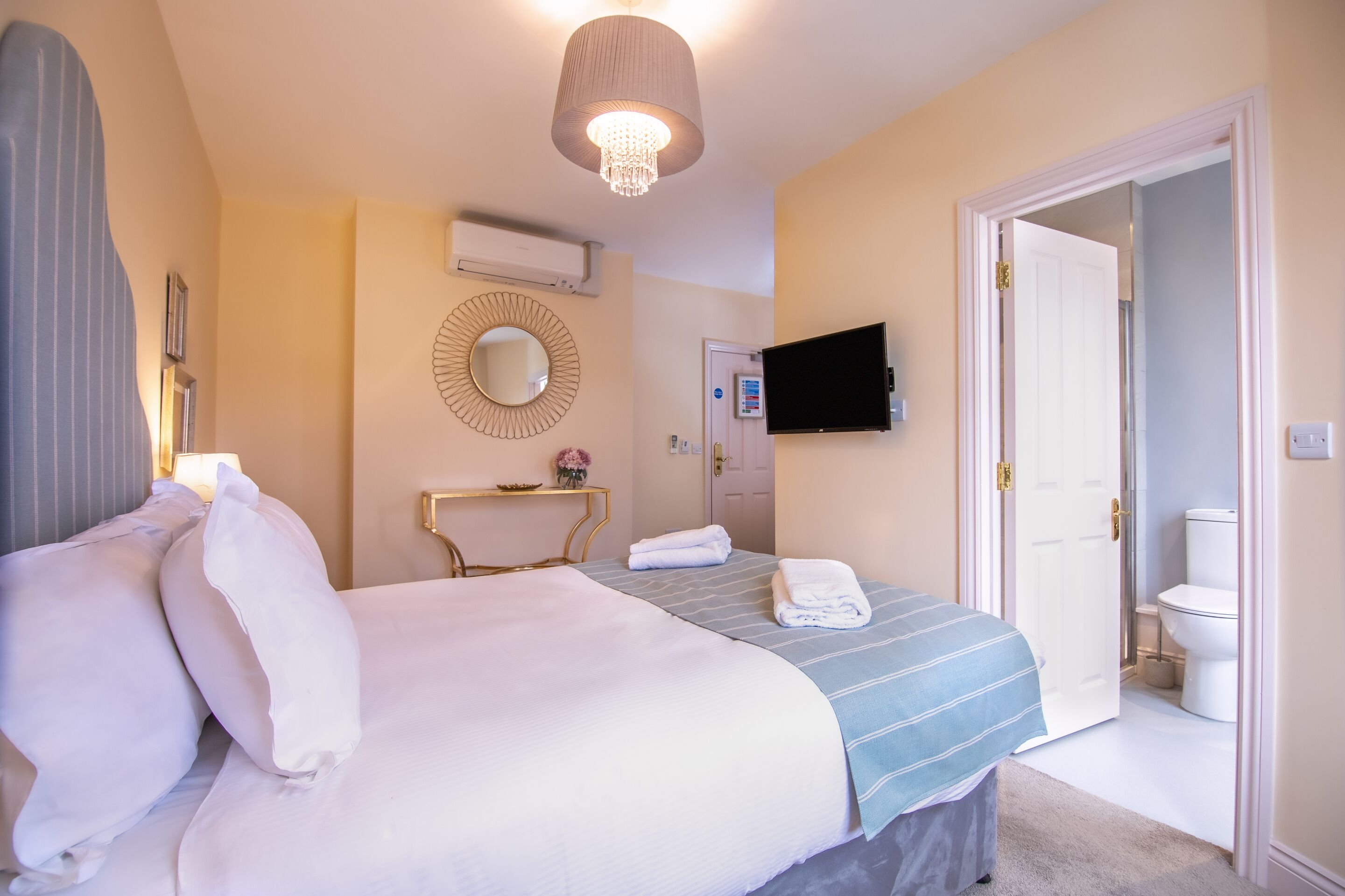 Une chambre d’hôtel avec un lit, une table de chevet, une télévision et une salle de bain visible à travers une porte ouverte.