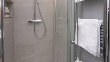 Un área de ducha con paredes de vidrio, suelo de azulejos blancos y puerta de vidrio.