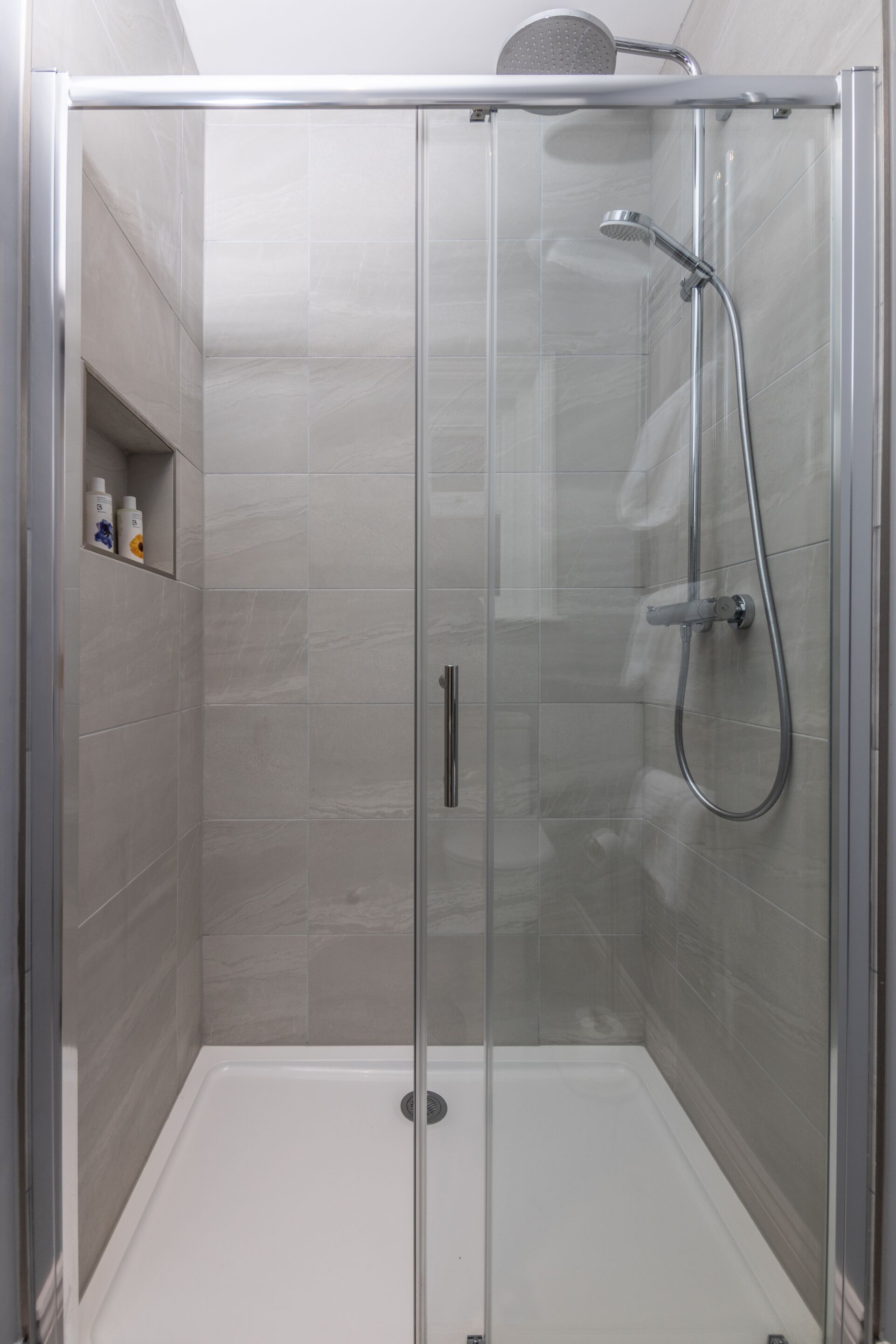 A glass-enclosed shower stall with a handheld showerhead and a wall-mounted faucet.