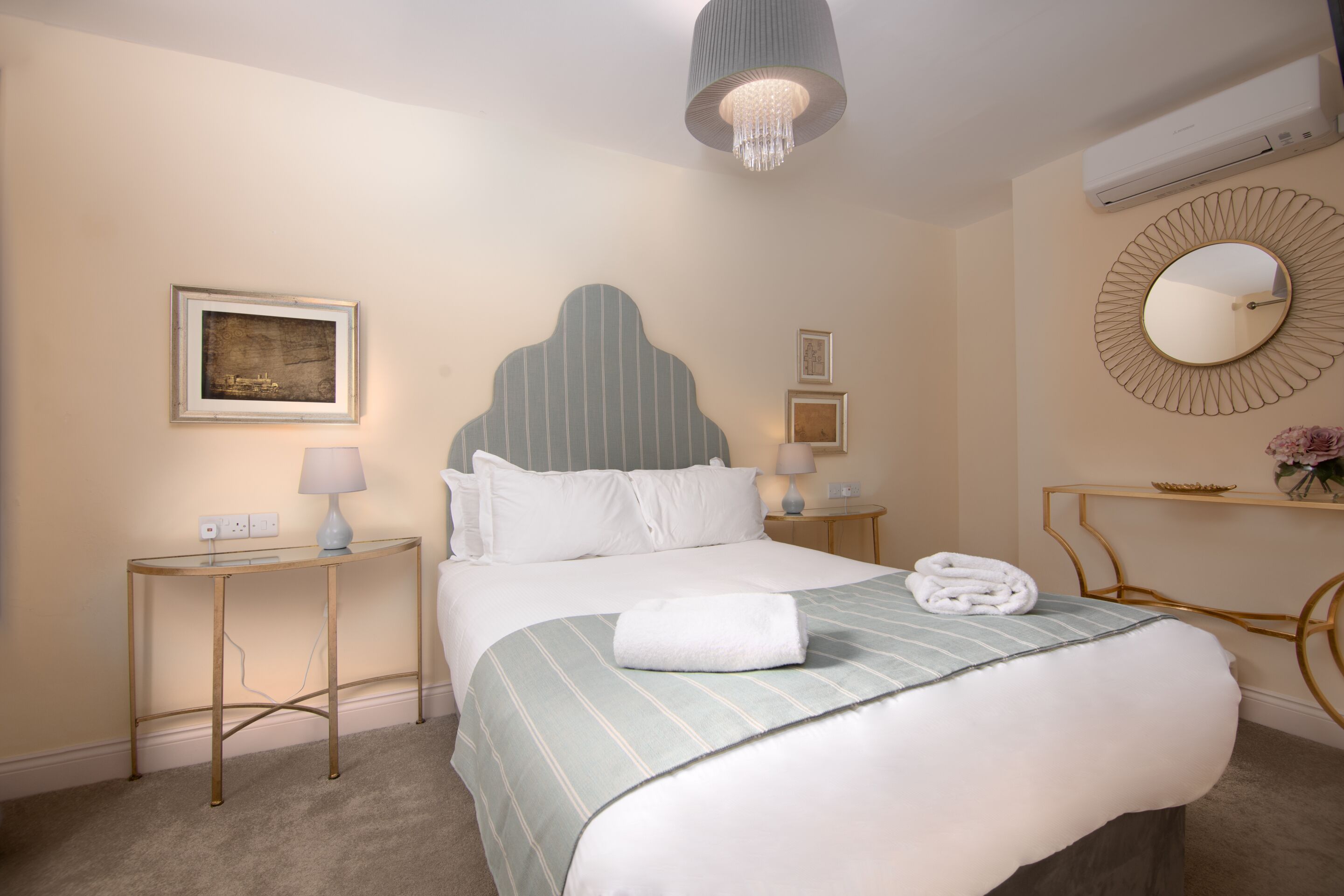 Una camera d'albergo ordinata con un letto, comodini, una lampada, uno specchio e opere d'arte alle pareti.