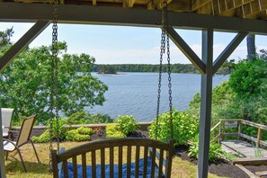 A wooden swing chair overlooking a lake with a view of the shoreline and a dock. - Amazing pond views and unforgettable sunsets from all levels! (Dennis Port)