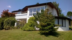 Una casa de dues plantes amb un balcó, envoltada de gespes ben cuidades i diversos arbres.