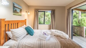 Un dormitorio con cabecera de madera, cama con ropa de cama a rayas, un cuadro en la pared y una ventana con cortinas.