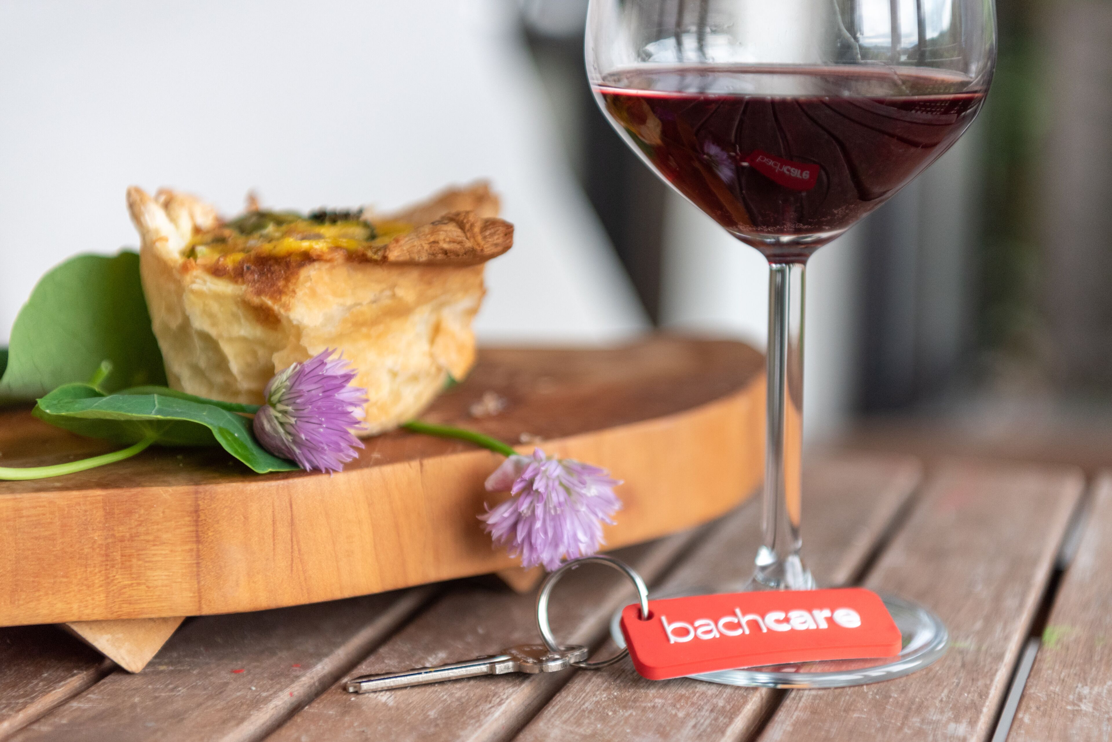 A wooden table with a glass of red wine, a keychain with a red tag, and a pastry on a wooden board.