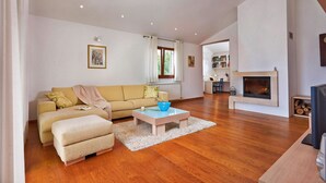 A spacious living room with a sofa, ottoman, coffee table, fireplace, and a view of the kitchen. - Villa Theresa in Ližnjan (Haus für 12 Personen) (Liznjan)