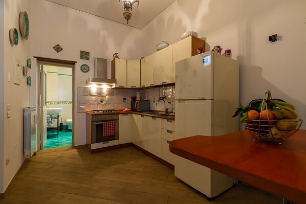 A compact kitchen with white cabinets, a red countertop, and a refrigerator. A fruit bowl is on the countertop.