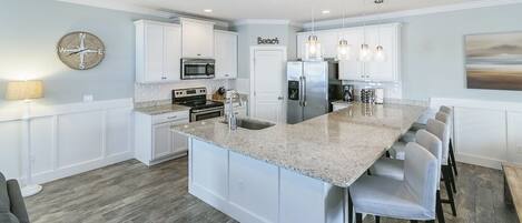 A modern kitchen with white cabinetry, a large island, stainless steel appliances, and pendant lighting.