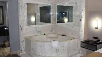 A bathroom with a marble bathtub, two wall-mounted mirrors, and a small bedside table with a lamp.