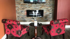 Une pièce avec un téléviseur fixé au mur en briques, deux fauteuils à motifs floraux et une petite table ronde.
