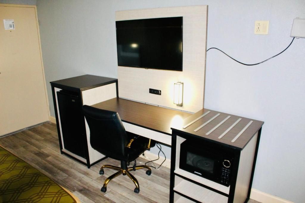 A compact room with a desk, chair, television, and microwave.
