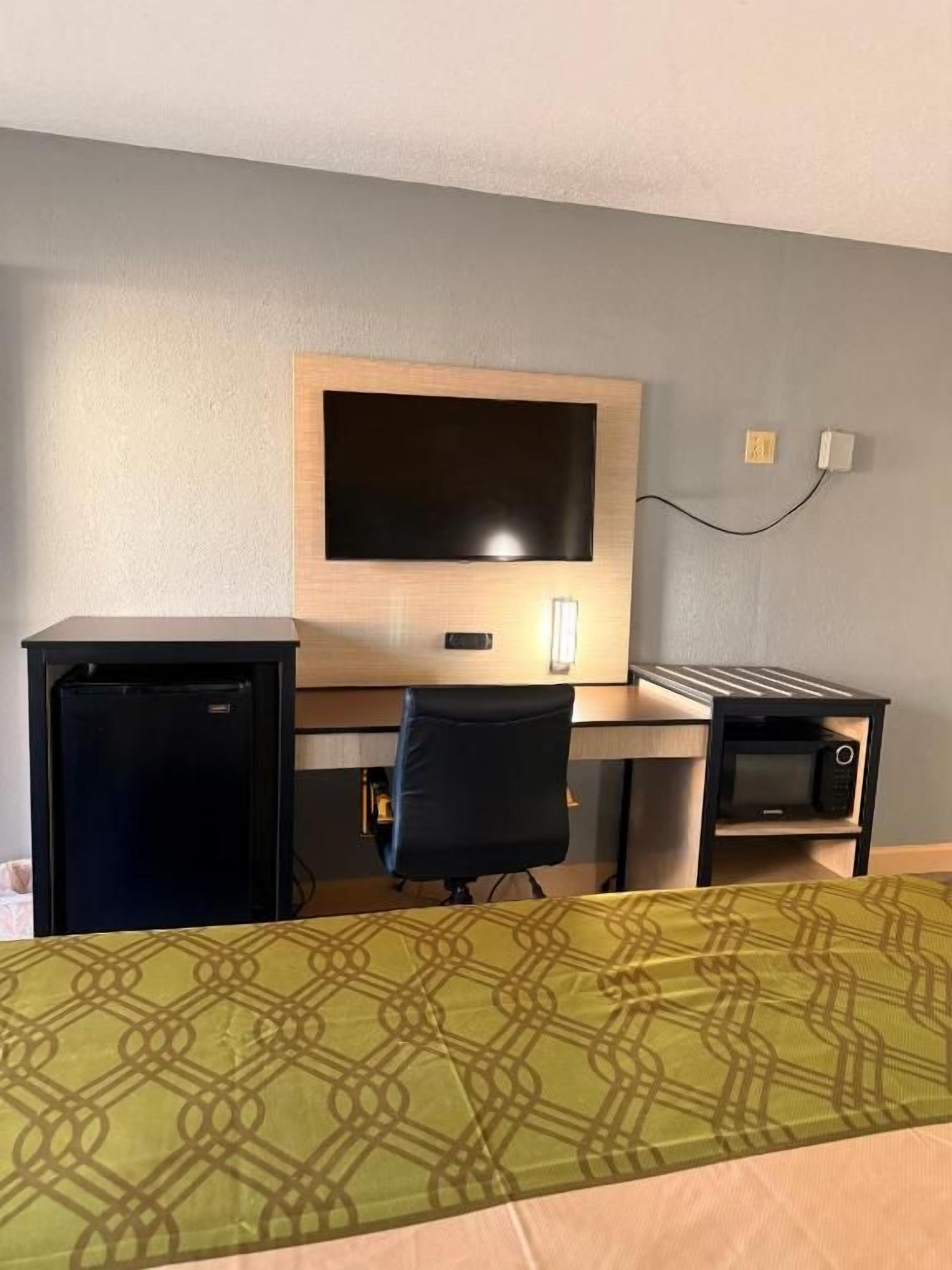 Una habitación de hotel con una cama, un escritorio, un televisor, un refrigerador y un microondas.