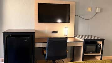 Una habitación de hotel con una cama, un escritorio, un televisor, un refrigerador y un microondas.
