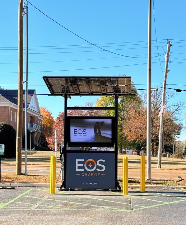 A charging station with a solar panel roof, labeled 'EOS CHARGE', and a screen displaying 'EOS LINX'. - Milan Inn & Suites (Milan)