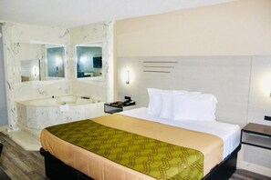 A hotel room with a bed, a large mirror, a bathroom with a bathtub, and a nightstand.