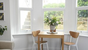 A room with a corner table, two chairs, a small round table with a book and a decorative bird, and a colorful rug. - Charming one bed  flat near Brighton Station and short walk to North Laine (Brighton)