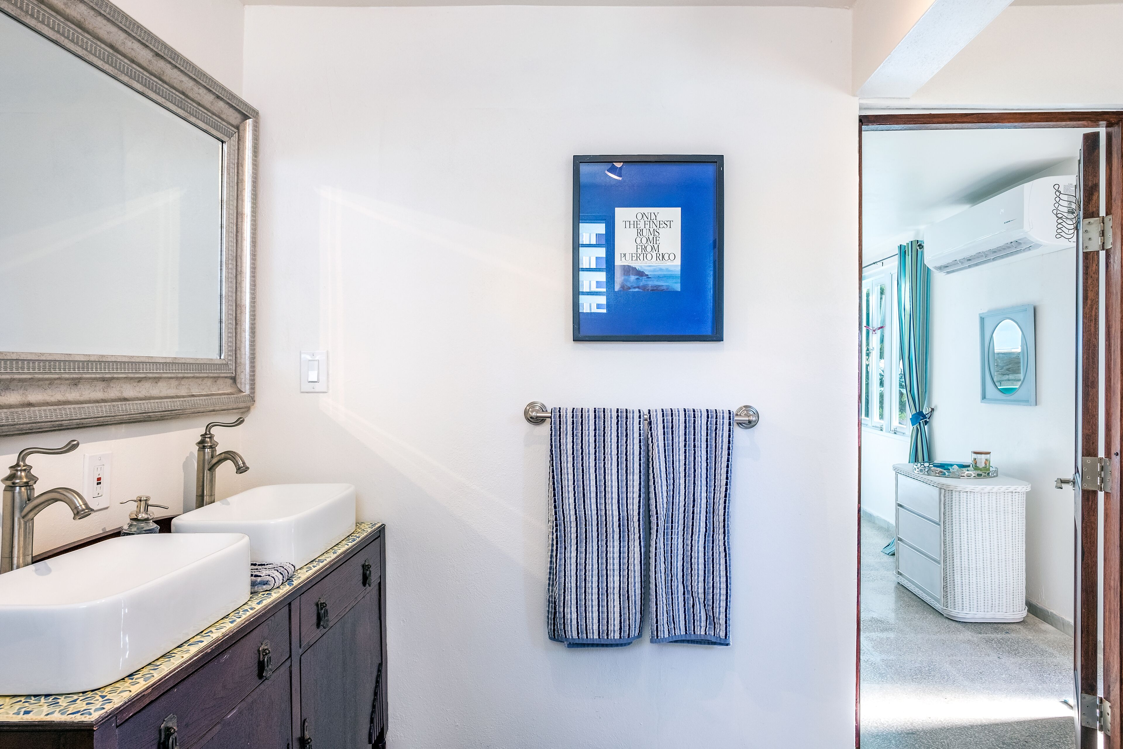 Une salle de bain avec deux lavabos, un miroir, un porte-serviettes avec une serviette à rayures et un tableau encadré au mur.