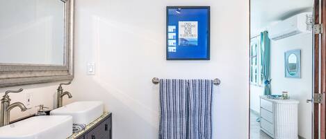 Une salle de bain avec deux lavabos, un miroir, un porte-serviettes avec une serviette à rayures et un tableau encadré au mur.