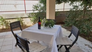 Ett bord dukat utomhus med en vinflaska, glas och en vas med blommor.