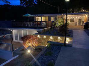 Uma casa moderna com um deck, um caminho de pedra e uma área de jardim bem iluminada.