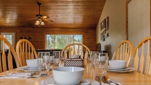 Comedor con mesa de madera dispuesta para cuatro, con fuentes, vasos y cubiertos.