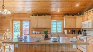 Cocina de cabaña de madera con una isla central, armarios de madera y una zona de comedor con sillas.