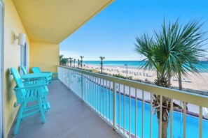 A balcony with a pool, turquoise chairs, and a view of the beach.