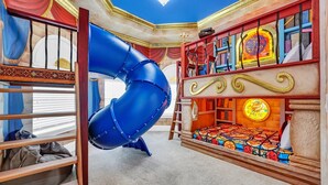 A room with a bunk bed, a blue slide, and a colorful stained glass window. - Ultimate Family Getaway | Game Room/Movie Theater, Private Pool, Custom Themed Rooms (Kissimmee)