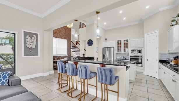 A modern kitchen with a central island, bar stools, and a dining area with a grey sofa. - Ultimate Family Getaway | Game Room/Movie Theater, Private Pool, Custom Themed Rooms (Kissimmee)