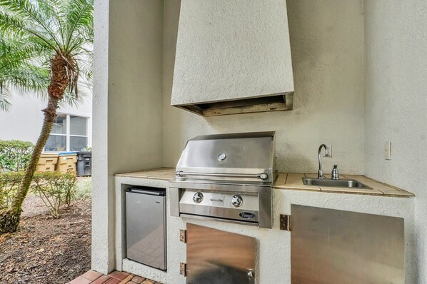 An outdoor kitchen with a built-in grill, a sink, and a compact refrigerator.