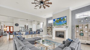 A spacious living room with a large gray sectional sofa, a glass coffee table, and a fireplace. - Ultimate Family Getaway | Game Room/Movie Theater, Private Pool, Custom Themed Rooms (Kissimmee)