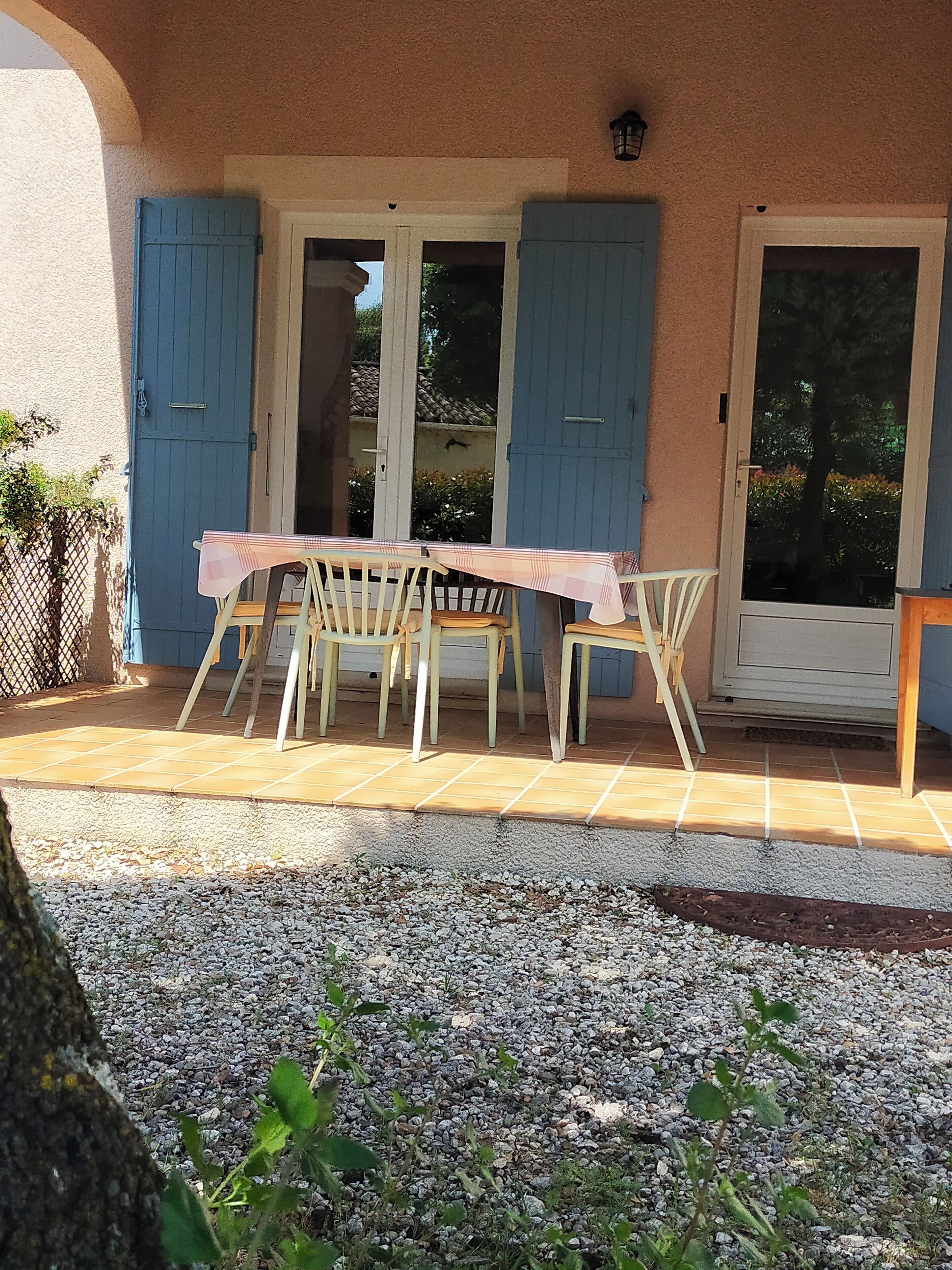 A patio area with a table and chairs, a door with blue shutters, and a gravel path.