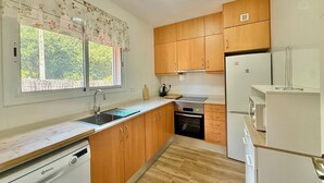 A compact kitchen with wooden cabinets, a built-in oven, a dishwasher, and a refrigerator. - Club Villamar - Nice house, complete and very sunny, located in a quiet urbanization,with a  priv... (Vidreres)